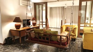 Una habitación de hotel con una silla colgante, un escritorio con lámpara, un televisor y una cama con cortinas.