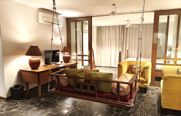 A hotel room with a swing chair, a desk with a lamp, a television, and a bed with curtains. - The Sky Imperial Aarivaa Luxury Homestay (Rajkot)