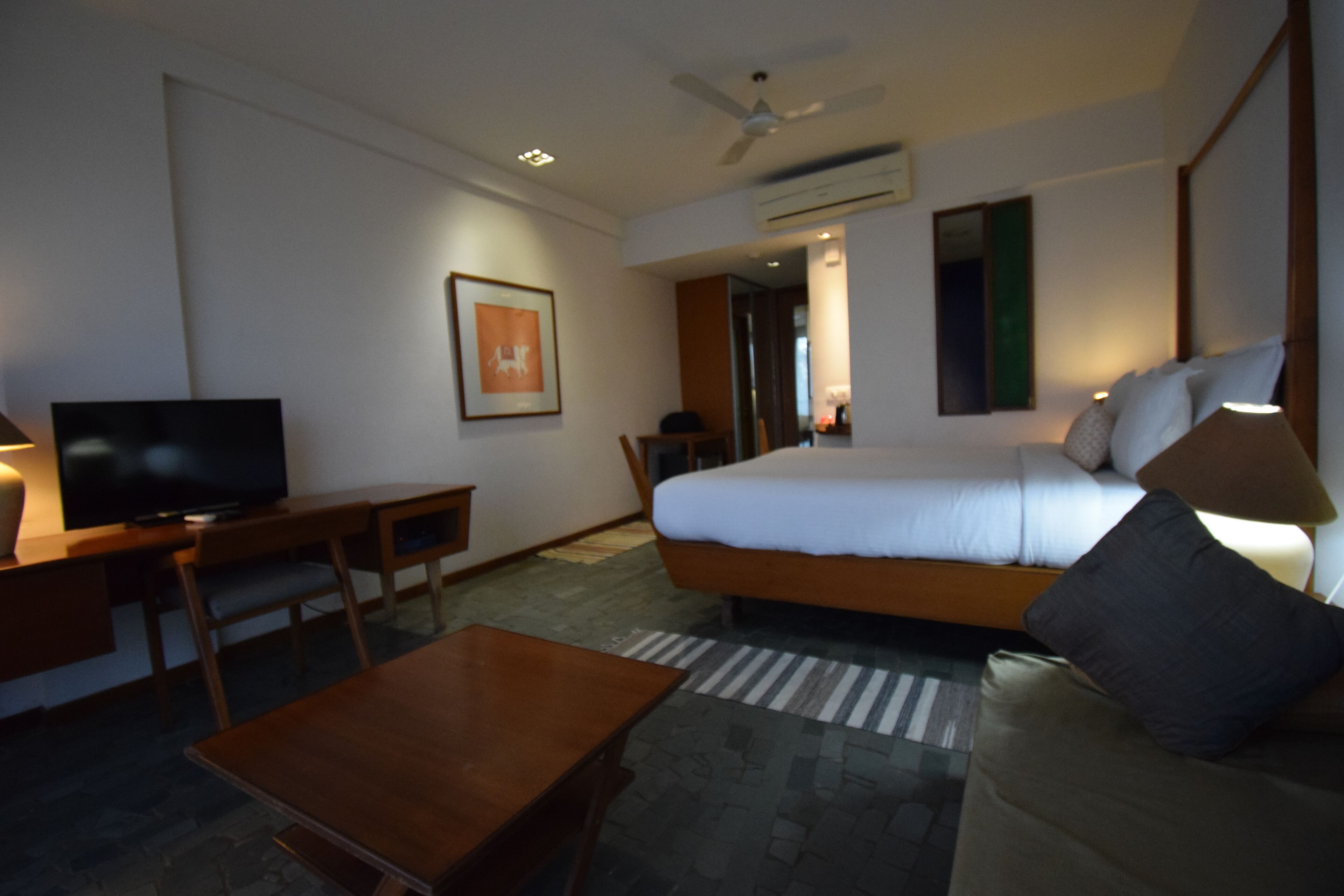 A hotel room with a bed, a desk, a television, and a ceiling fan.