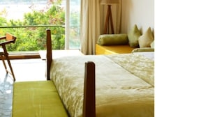 Habitación de hotel con cama, escritorio, silla, lámpara y vista a zonas verdes.
