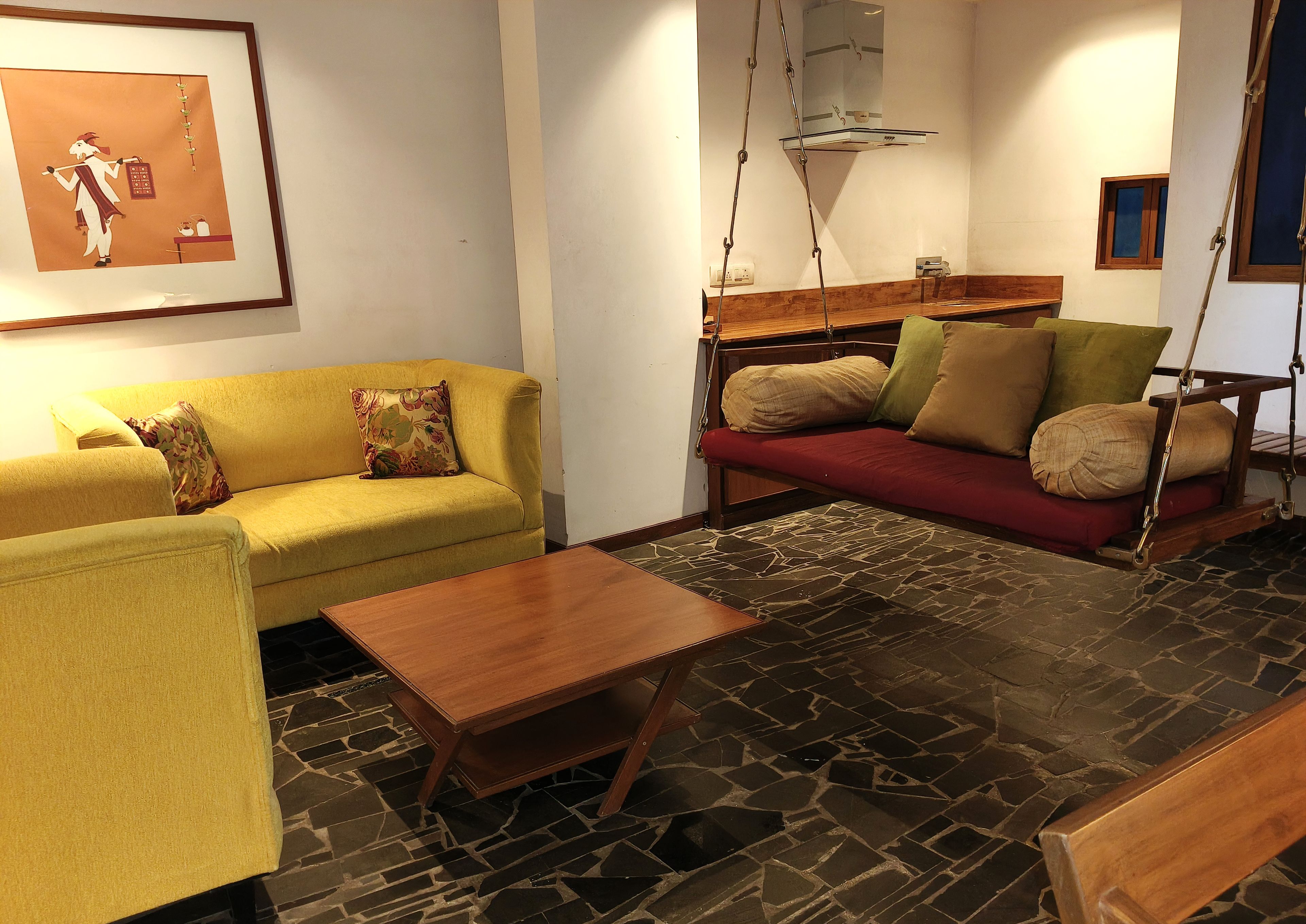 A living room with a yellow sofa, a red sofa, a wooden coffee table, and a swing chair.