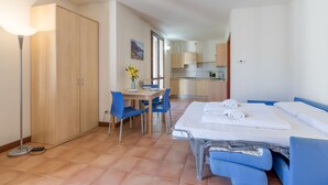 A room with a bed, a desk with chairs, a dining table, and a kitchenette.
