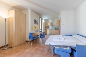 Hotellihuone, jossa on sänky, työpöytä, tuoleja, vaatekaappi ja pieni keittiö.