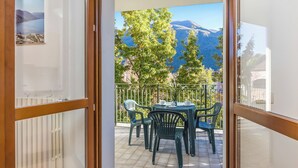 A balcony with a view of mountains and trees, a table with chairs, and a railing.