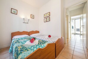 A neatly made bed with a patterned bedspread, a wooden headboard, and a single decorative flower.
