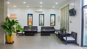 A reception area with a modern design, featuring a seating area with sofas and chairs, a large potted plant, and framed cityscape pictures on the wall. - Angkor Vattanakpheap Villa (Siem Reap)