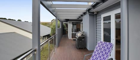 A covered balcony with a grill, a lounge chair, and a view of the neighborhood.