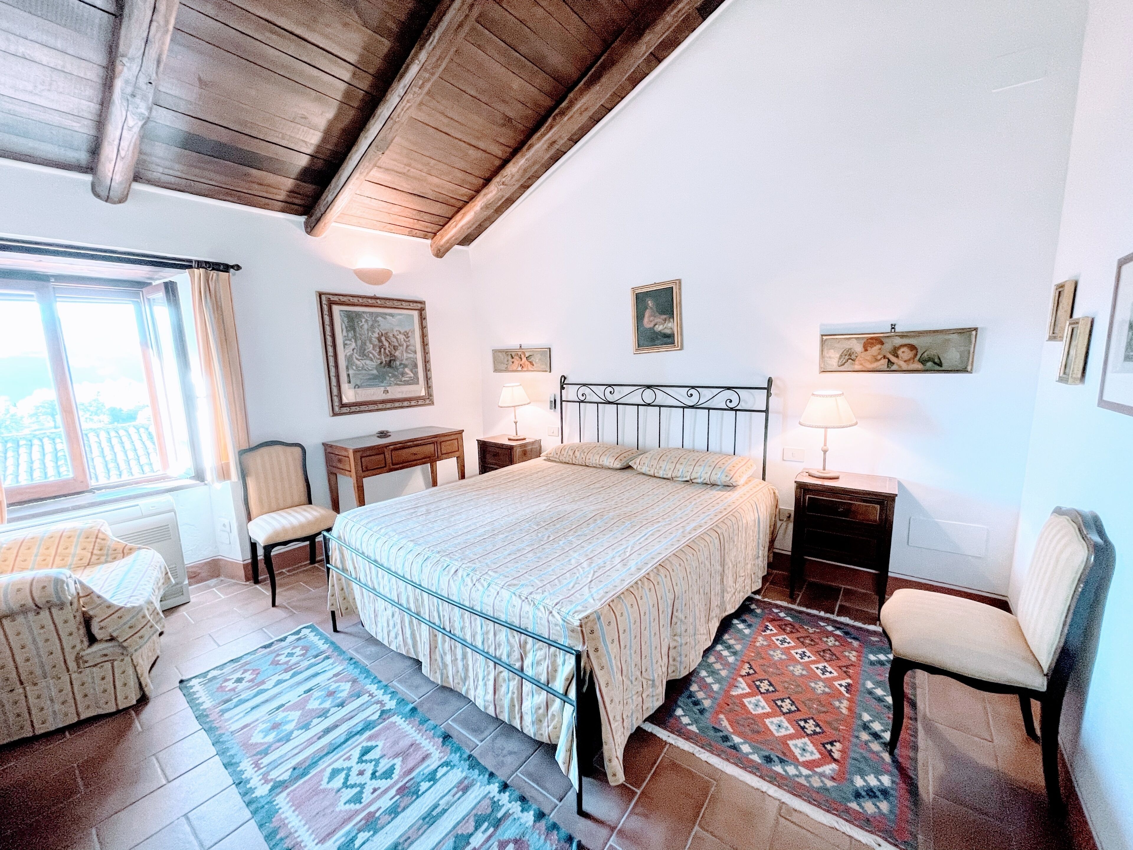 Une chambre à coucher avec un lit, deux tables de chevet, une chaise, une fenêtre et une vue sur l’extérieur.