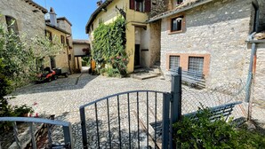 A cobblestone courtyard with stone buildings, a metal gate, and a bench. - Vicolo - sleeps 5 with air con, wifi, balcony for dining and pool (Umbria)