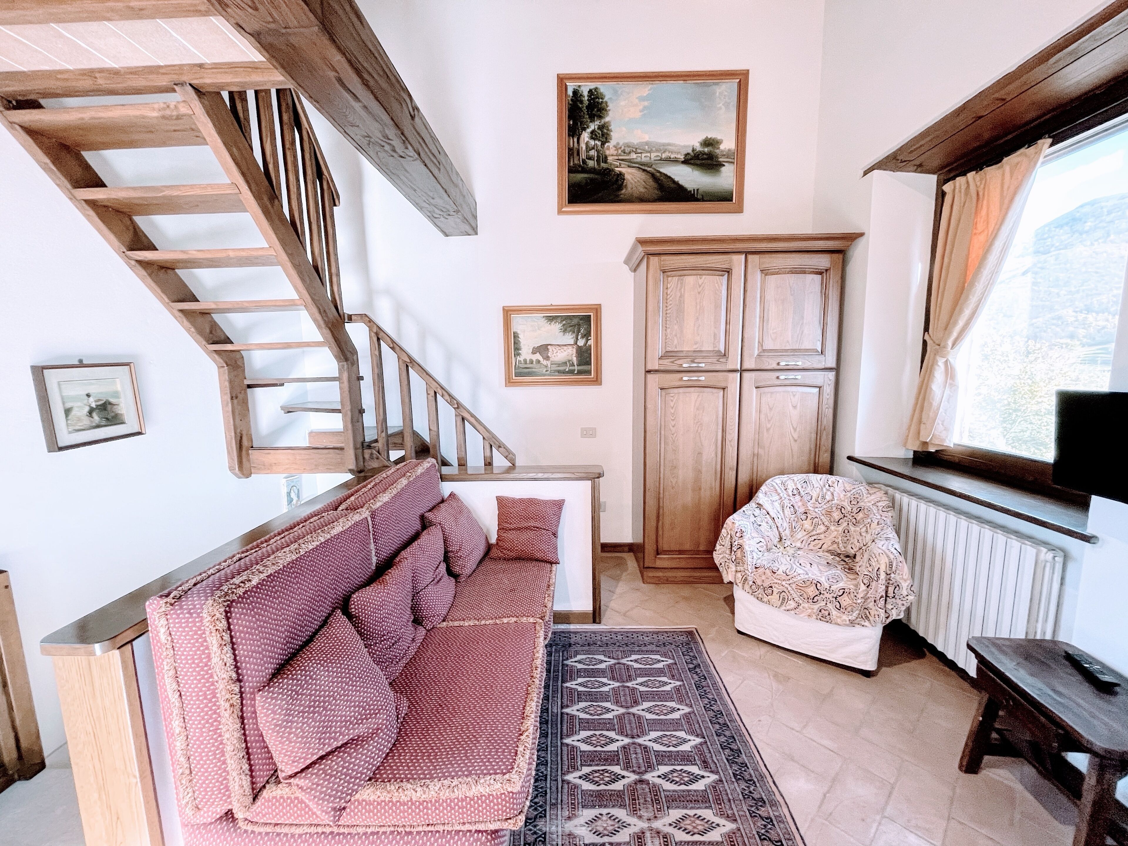 A living room with a staircase, a sofa, a cabinet, and a window.