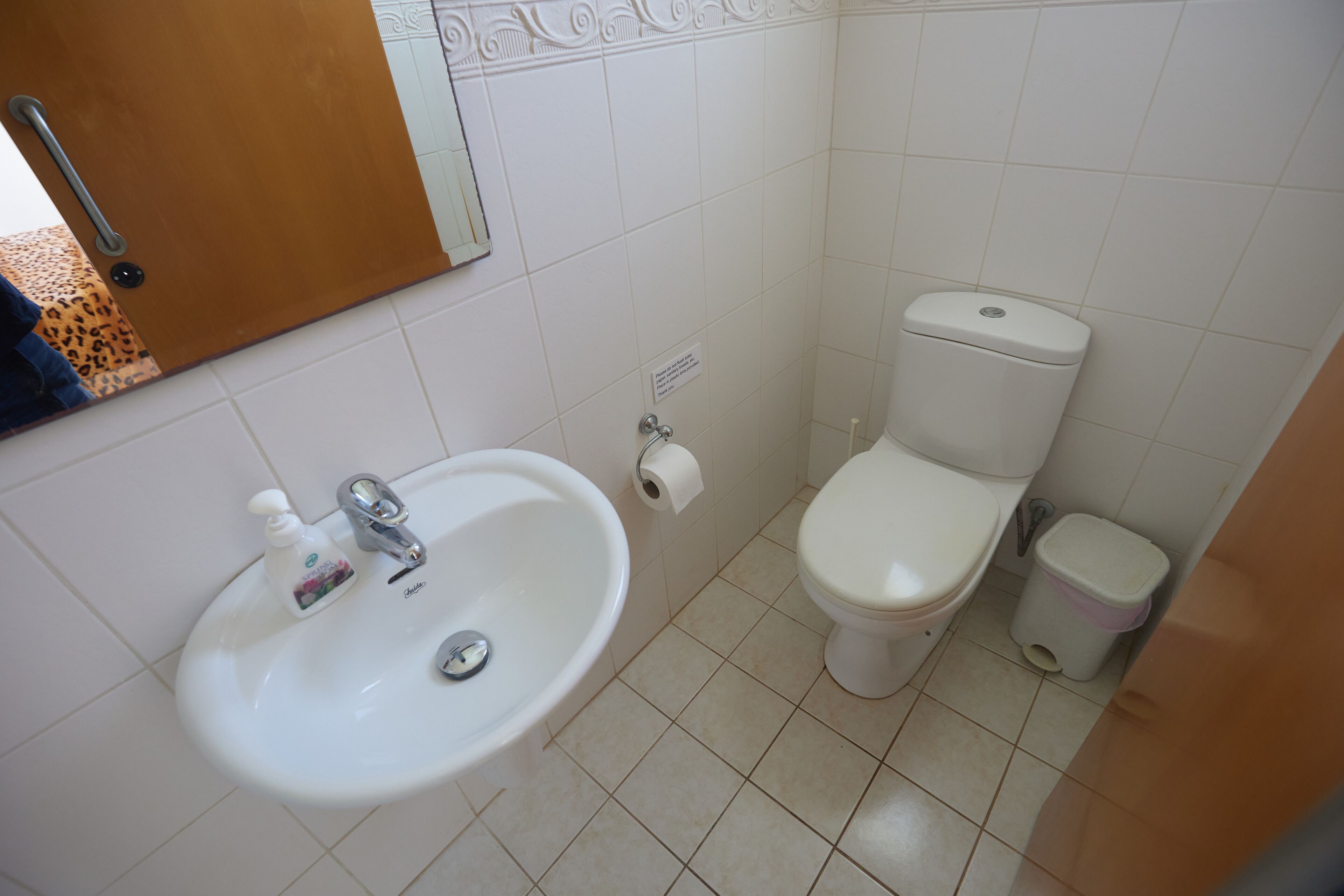 A bathroom with a sink, toilet, and trash bin.