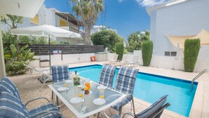 A poolside area with a glass table, blue plaid chairs, and a white umbrella. - Protaras Delfini Villa Dv4 (Protaras)