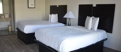 A hotel room with two beds, a bedside table with a lamp, a framed picture on the wall, and a mirror above the door.
