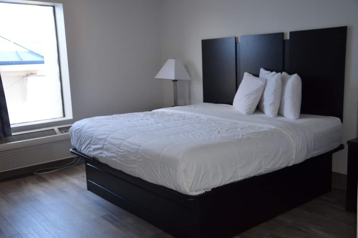 Quarto de hotel moderno com uma cama grande, mesa de cabeceira, abajur e janela com persianas.