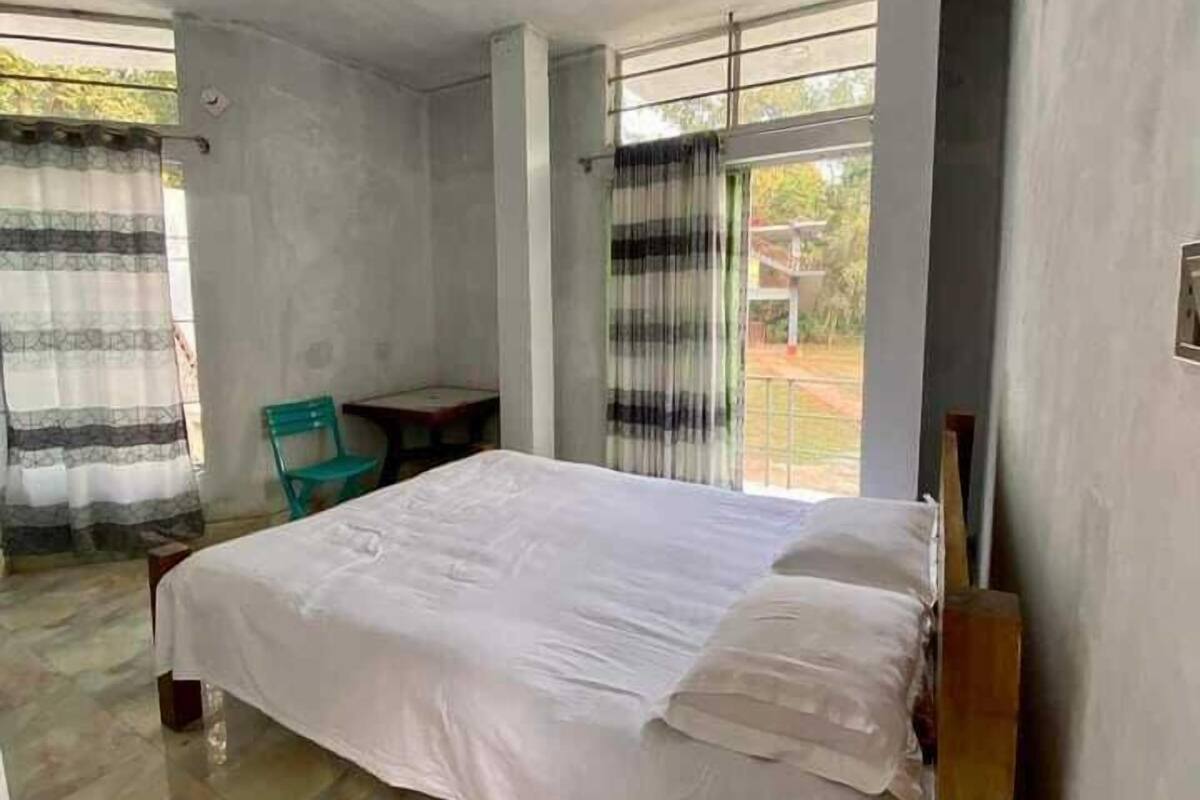 A room with a bed, a chair, a small table, and large windows.
