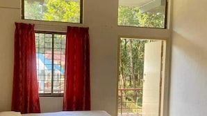 Un dormitori amb un llit, una finestra amb cortines vermelles i vista a un edifici i arbres a l'exterior.