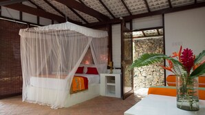 Una habitación con cama bajo un dosel, pared de piedra y mesa con un florero.