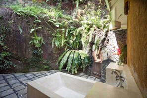 Un baño con pared de piedra, una bañera grande y diversas plantas.