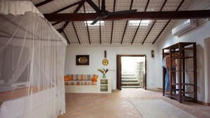 Una habitación amplia con techo alto, una cama con dosel, un sofá, una mesita con un florero y una escalera que da al exterior.
