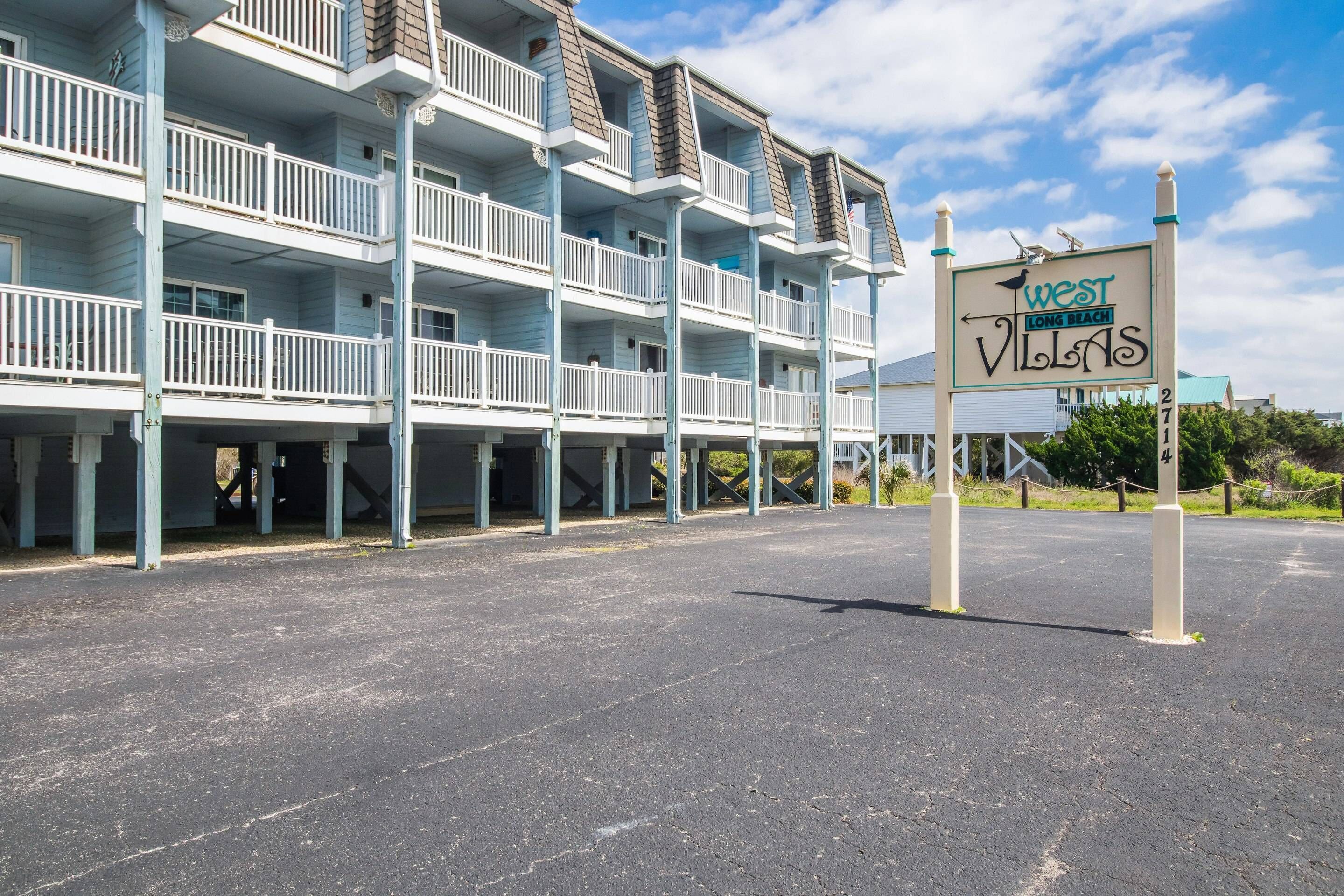 A multi-story building with balconies, a sign indicating 'West Long Beach Villas', and a parking area in front.