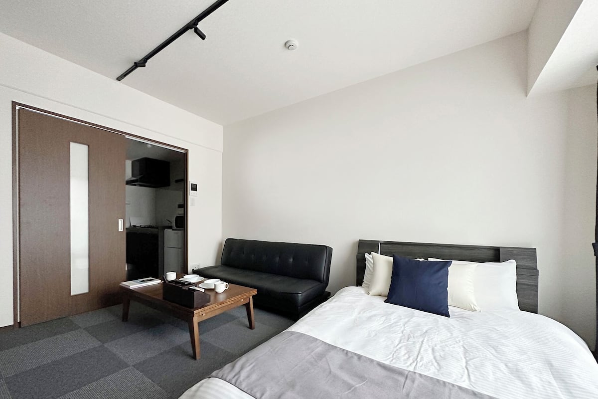 A hotel room with a bed, a sofa, a small table, and a kitchenette area.