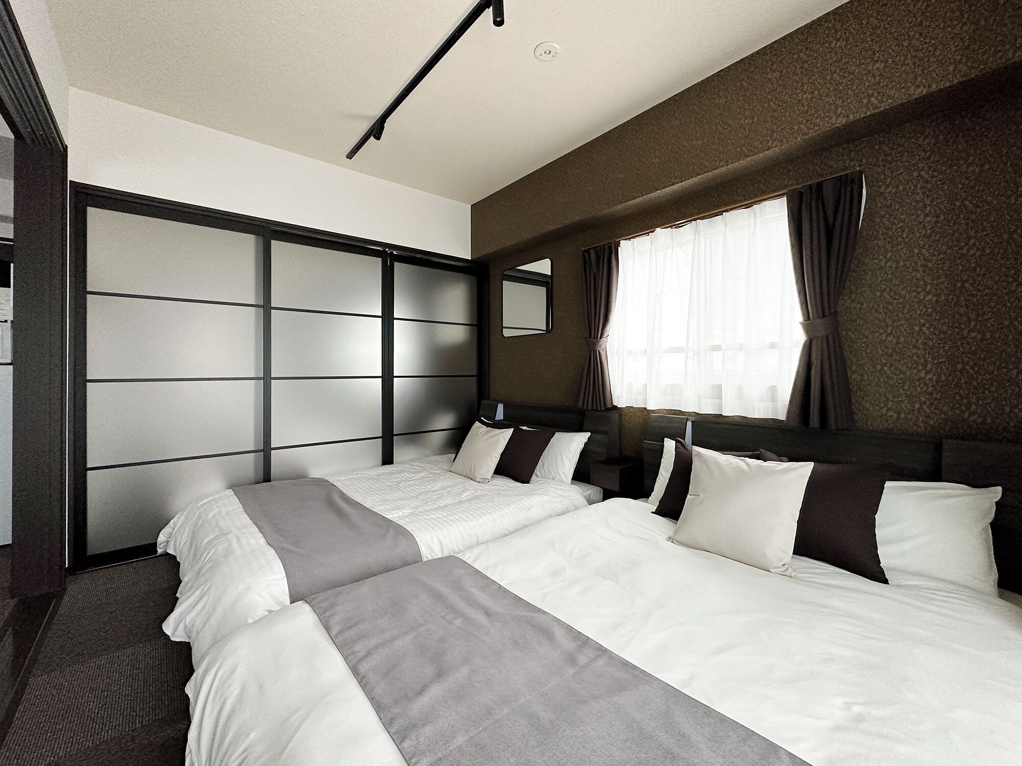 Habitación de hotel con dos camas, un ventanal grande con cortinas, un cabecero con espejo y una pared con textura.