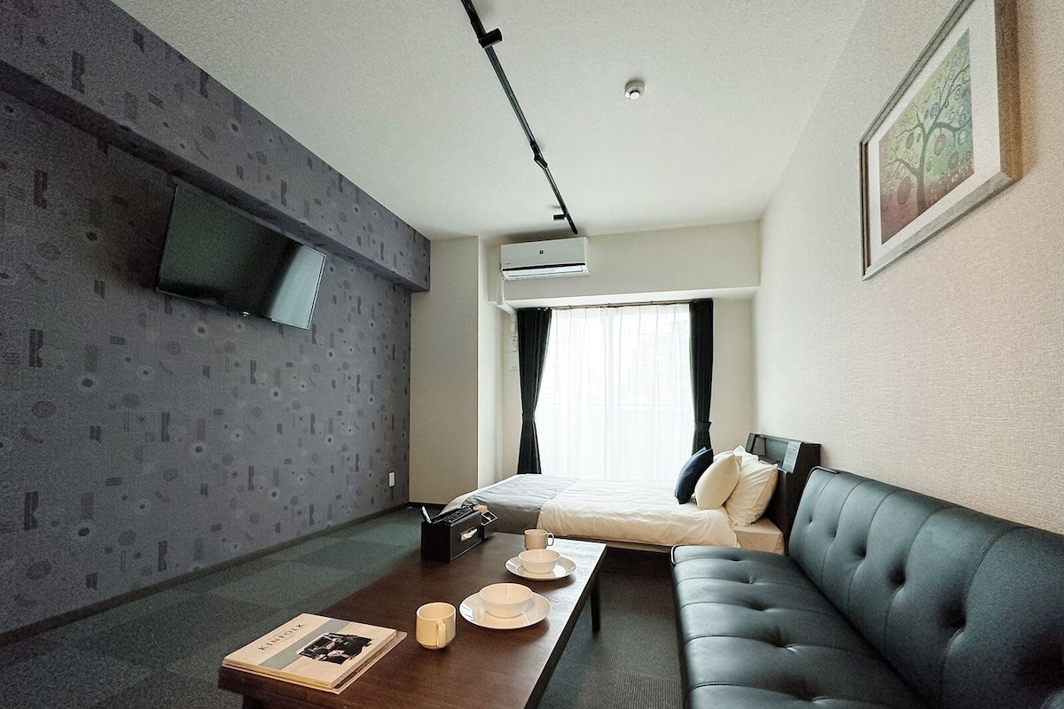 A modern hotel room with a bed, a sofa, a coffee table, and a TV mounted on the wall.