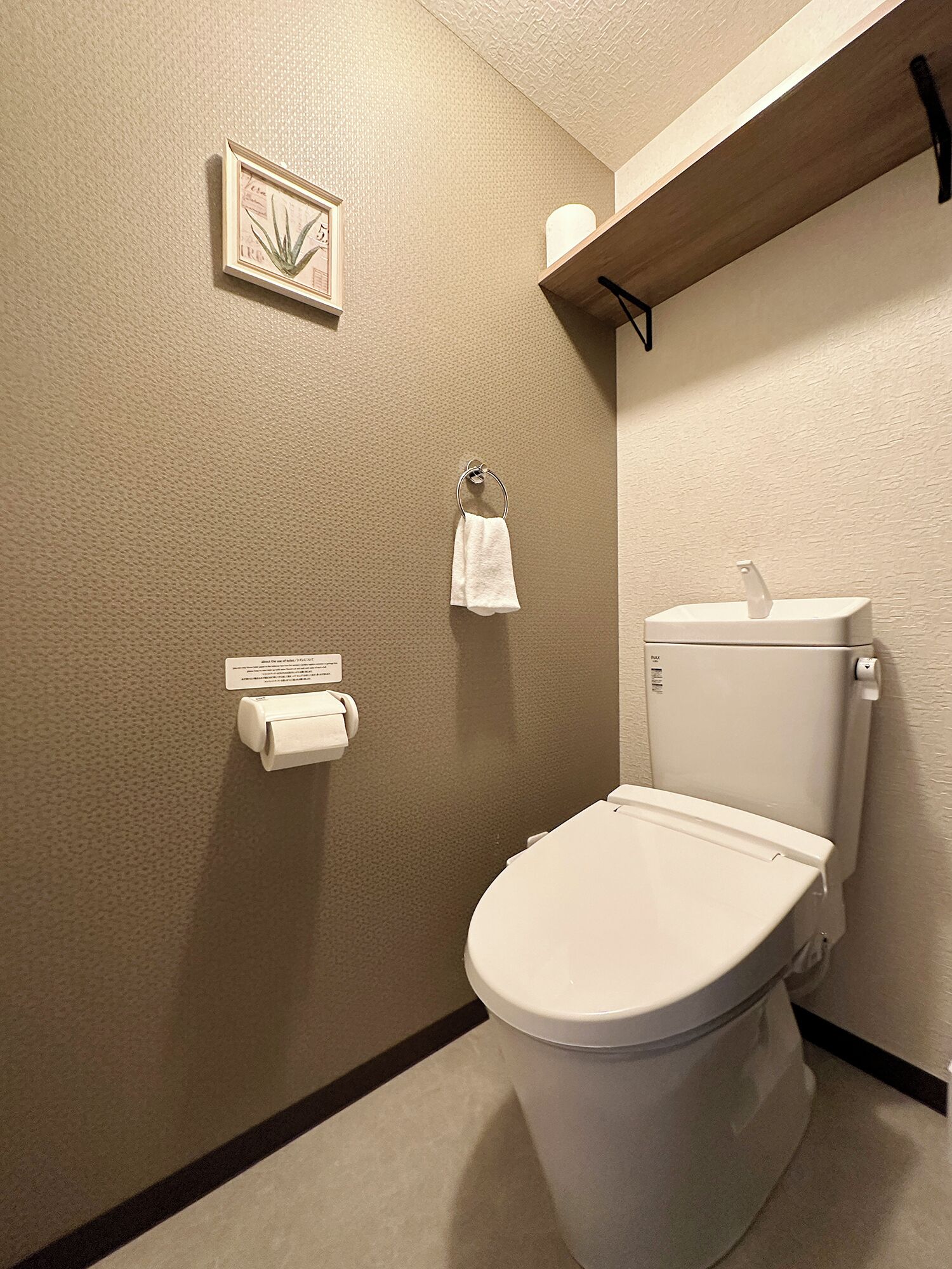 A small, modern bathroom with a toilet, a towel rack, a toilet paper holder, and a shelf with a roll of toilet paper.