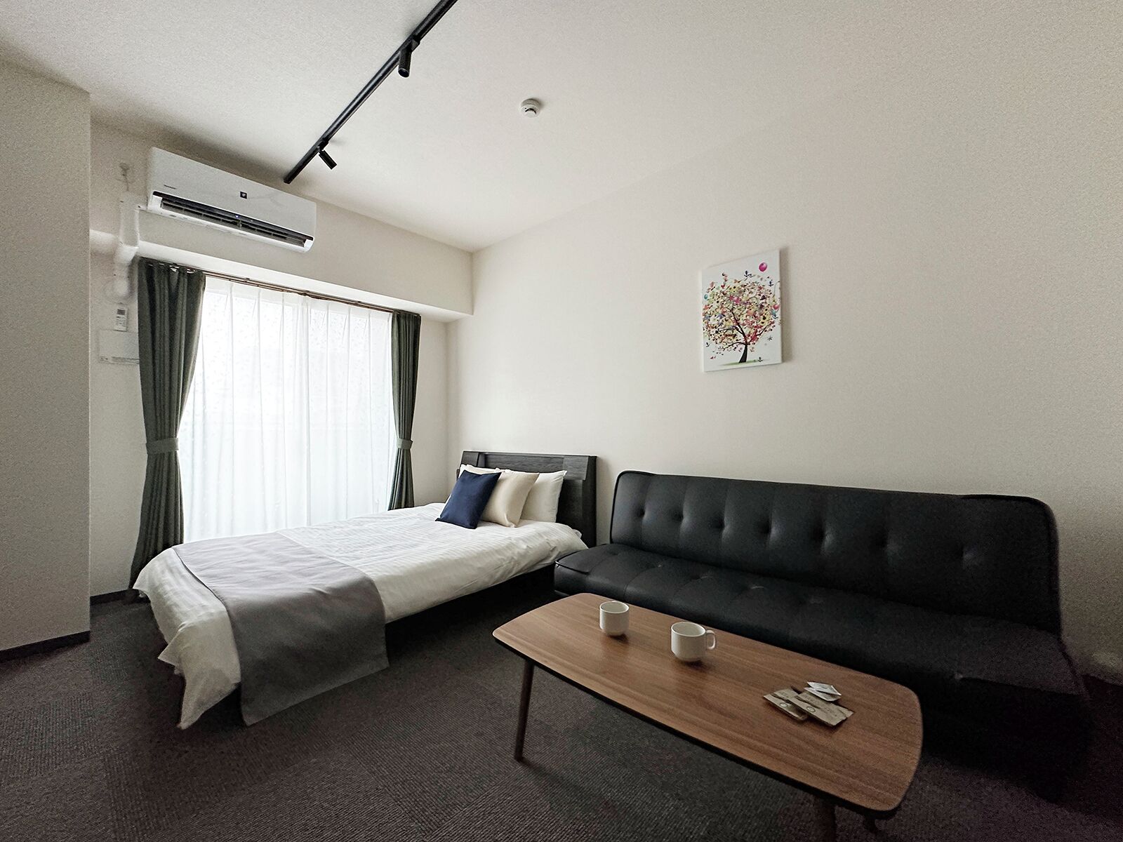 A hotel room with a bed, a black sofa, a wooden coffee table, and a painting on the wall.