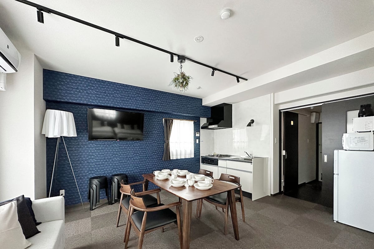A modern kitchen with white appliances, a dining area with a wooden table and chairs, and a blue textured wall.