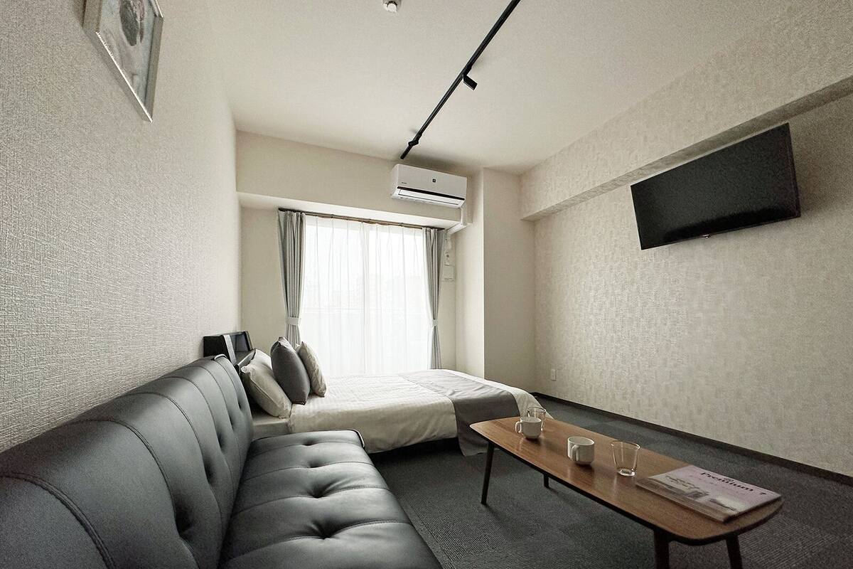 A hotel room with a sofa, a bed, a small table, and a TV mounted on the wall.