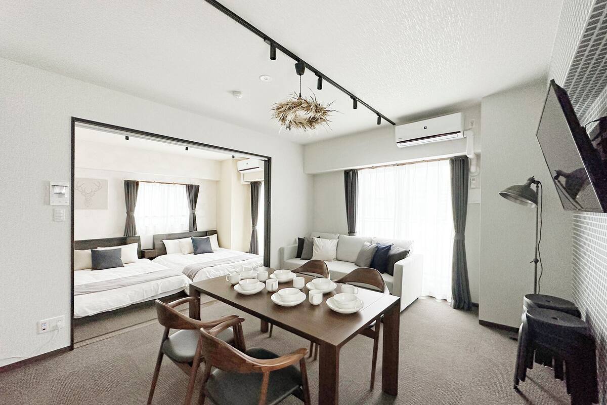 A modern hotel room with a large bed, a dining table with chairs, a TV, and a ceiling fan.
