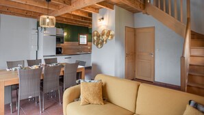 Una cocina moderna con vigas de madera, un comedor con sillas de mimbre y una escalera.