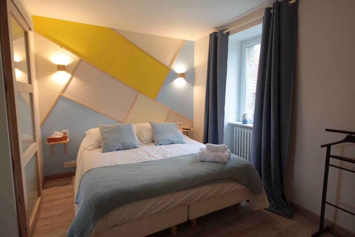Une chambre à coucher avec un lit, des tables de chevet, une fenêtre avec des rideaux et un radiateur.