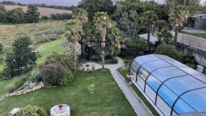 Un jardín con un invernadero de cristal, un sendero de piedra y diversas especies de árboles y arbustos.