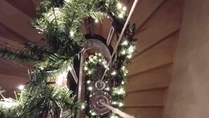 Un árbol de Navidad con luces y adornos, una escalera y cuadros en la pared.