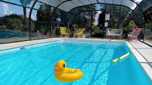 Piscina con un pato inflable amarillo, sillas de descanso y un porche cubierto.