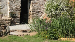 Un edificio de piedra con un acceso, rodeado de un jardín con diversas plantas y flores.