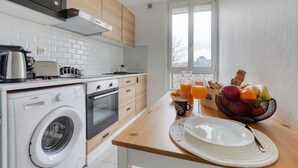 Een moderne keuken met een wasmachine, een koffiezetapparaat en een ontbijtgedeelte met fruit en sinaasappelsap.