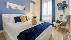 Een slaapkamer met een bed, een stoel, een nachtkastje, een wandplank met planten en een raam met gordijnen.