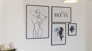 Een muur met vier ingekaderde kunstwerken, een kalender en een klein houten plankje met een kaars.