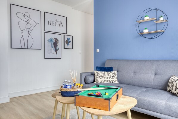 Un salon moderne avec un canapé gris, une table de billard et des œuvres d’art murales.