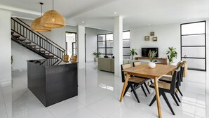 Un vaste espace de vie comprenant une grande table à manger, des chaises noires et en bois, un escalier et, au fond, une cuisine moderne.