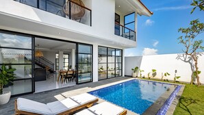 Une maison moderne à deux étages, dotée d’une piscine, de grandes fenêtres et d’un balcon aménagé avec du mobilier d’extérieur.