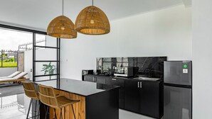 Une cuisine moderne avec des meubles de couleur noire, un réfrigérateur en acier inoxydable et une grande fenêtre donnant sur un jardin.
