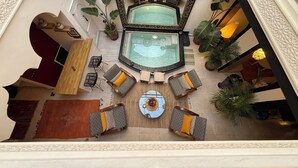 A luxurious indoor pool area with a central seating area, surrounded by various seating options and decorative plants. - Magnificent Riad Julilu Privatise in the heart of the Medina (11P) (Marrakech)