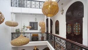 A multi-level interior with hanging wicker lamps, ornate doors, and a balcony with a wrought iron railing. - Magnificent Riad Julilu Privatise in the heart of the Medina (11P) (Marrakech)