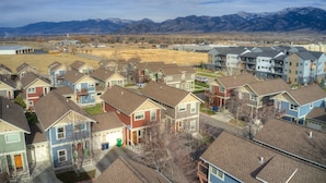 A residential area with multiple two-story houses, a clear sky, and mountains in the background.