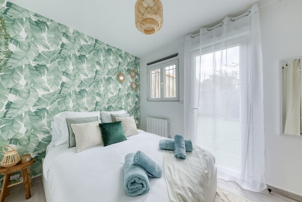 Ein Schlafzimmer mit Bett, Kissen, einem Fenster mit Vorhängen, einem Heizkörper und einer Wand mit Blättermuster.