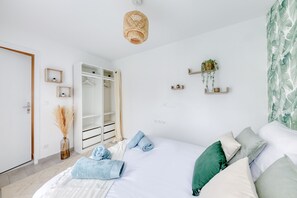 Ein modernes Schlafzimmer mit einem großen Bett, einem Kleiderschrank, einer Pendelleuchte und Wandregalen mit Pflanzen.